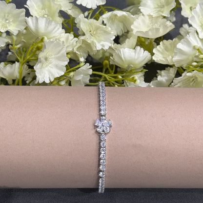 Silver bracelet with floral design on a beige surface with flowers in the background