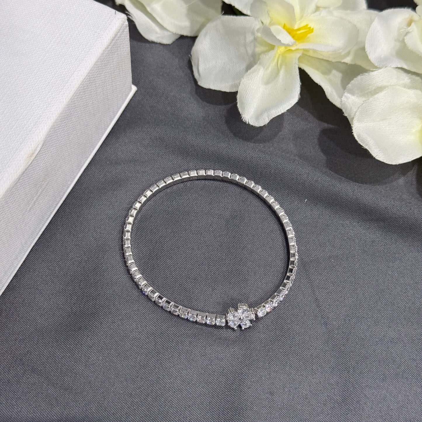 Silver bracelet with floral design on a gray surface with white flowers in the background