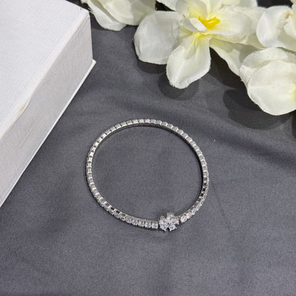 Silver bracelet with floral design on a gray surface with white flowers in the background