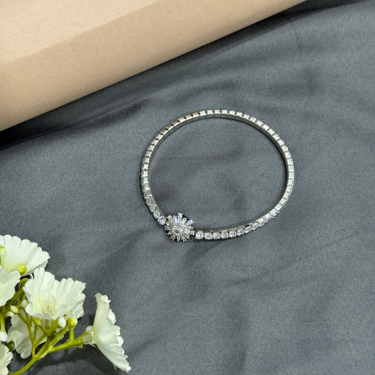 Silver bracelet with floral design on a gray fabric background with white flowers.