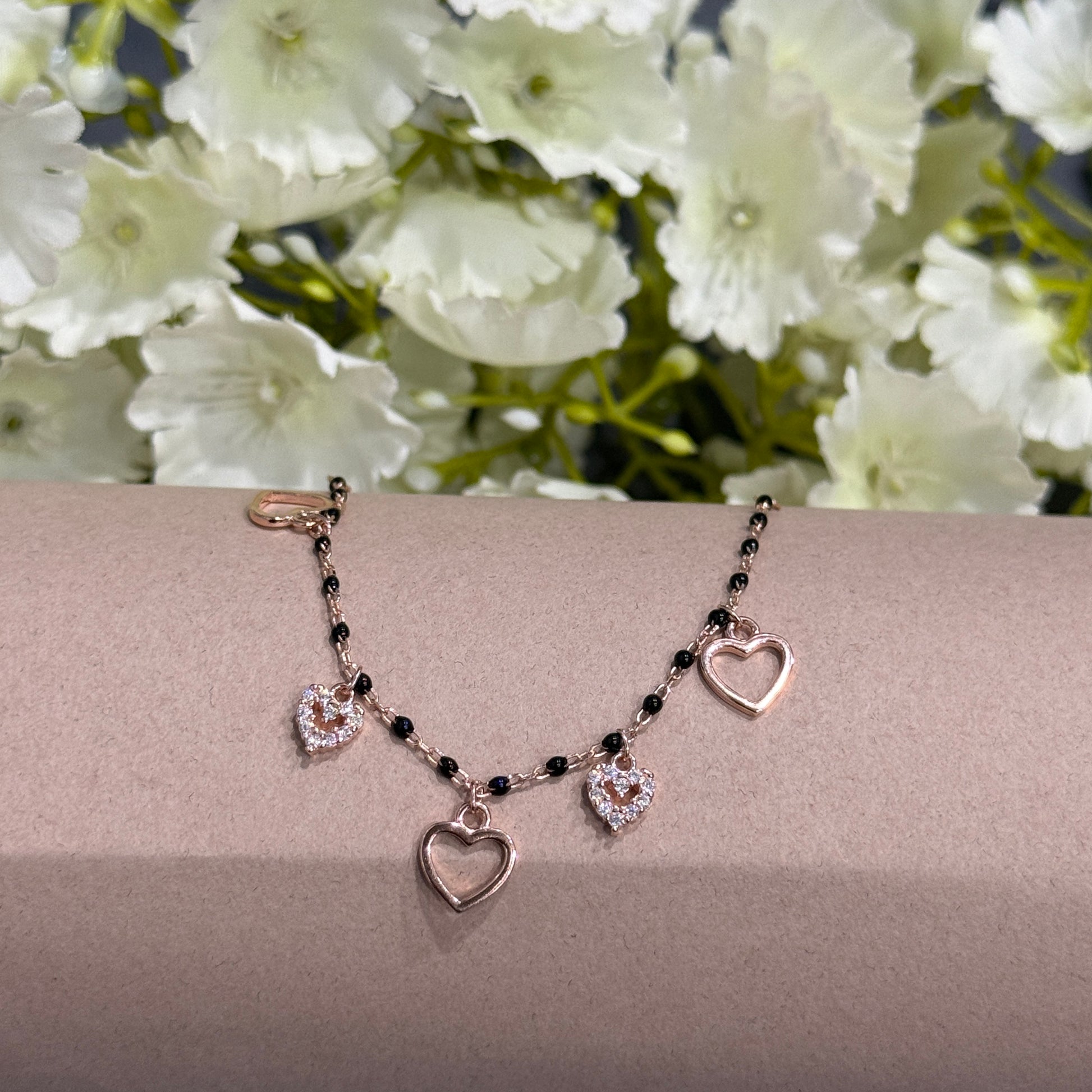 Necklace with heart-shaped pendants on a beige surface with white flowers in the background
