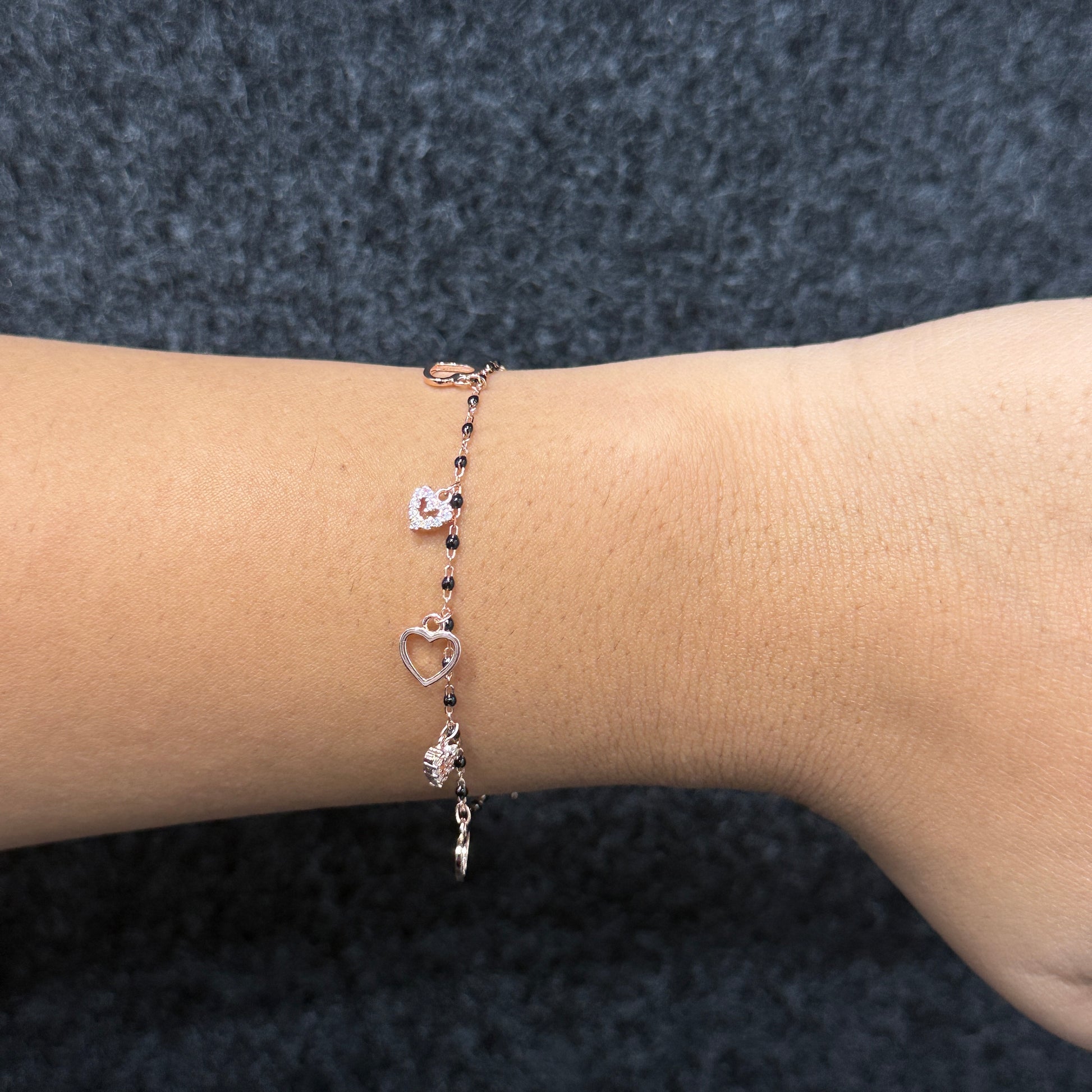 Bracelet with heart and flower charms on a wrist against a dark textured background