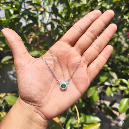 Hand holding a silver necklace with a green gemstone against a blurred green background