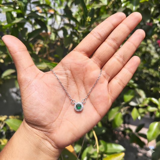 Hand holding a silver necklace with a green gemstone against a blurred green background