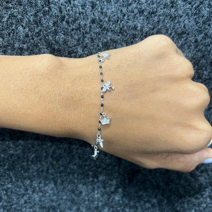 Silver bracelet with charms on a wrist against a dark background