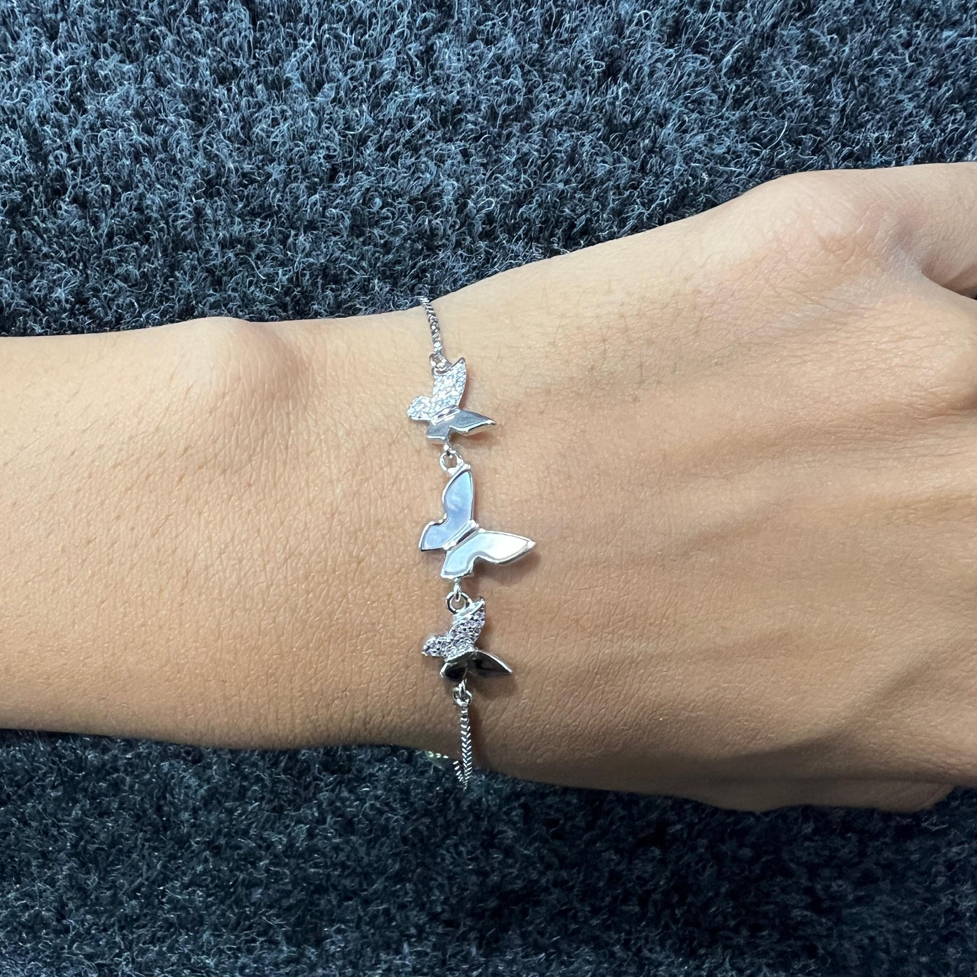 Silver butterfly bracelet on a wrist against a textured blue background