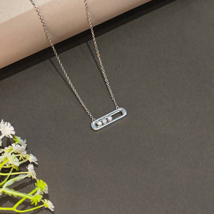 Silver necklace with a bar pendant on a dark surface with flowers.
