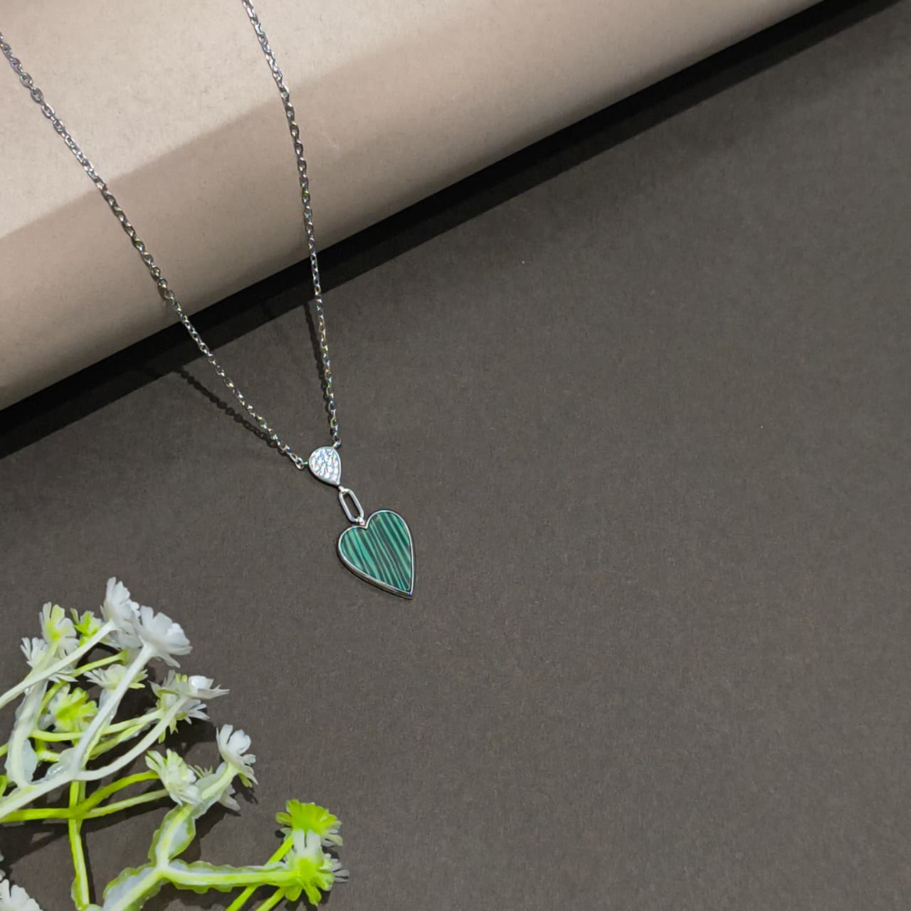 Necklace with a heart-shaped pendant on a gray surface with greenery