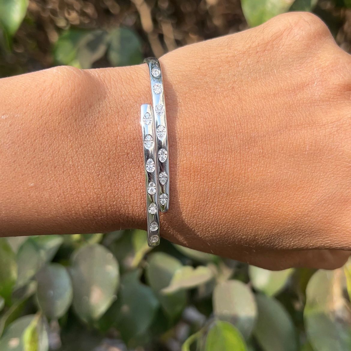 Silver bracelet on a wrist with a blurred green leafy background
