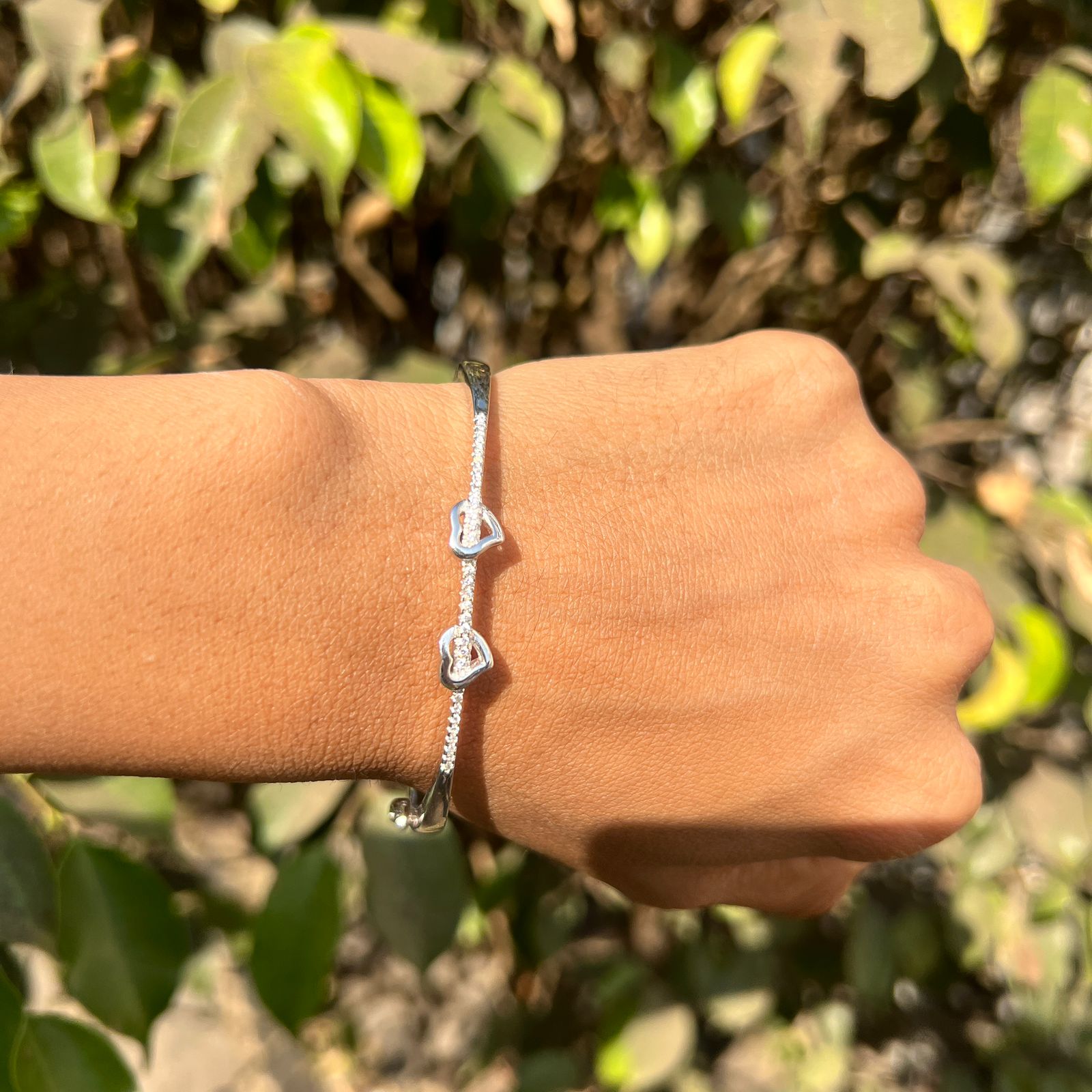 Silver bracelet on a wrist with a blurred green leafy background