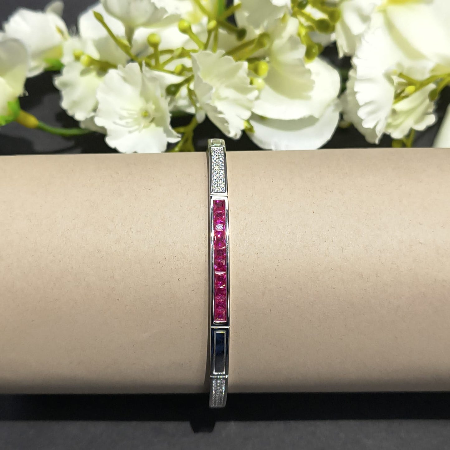 Bracelet with red stones on a beige surface with white flowers in the background