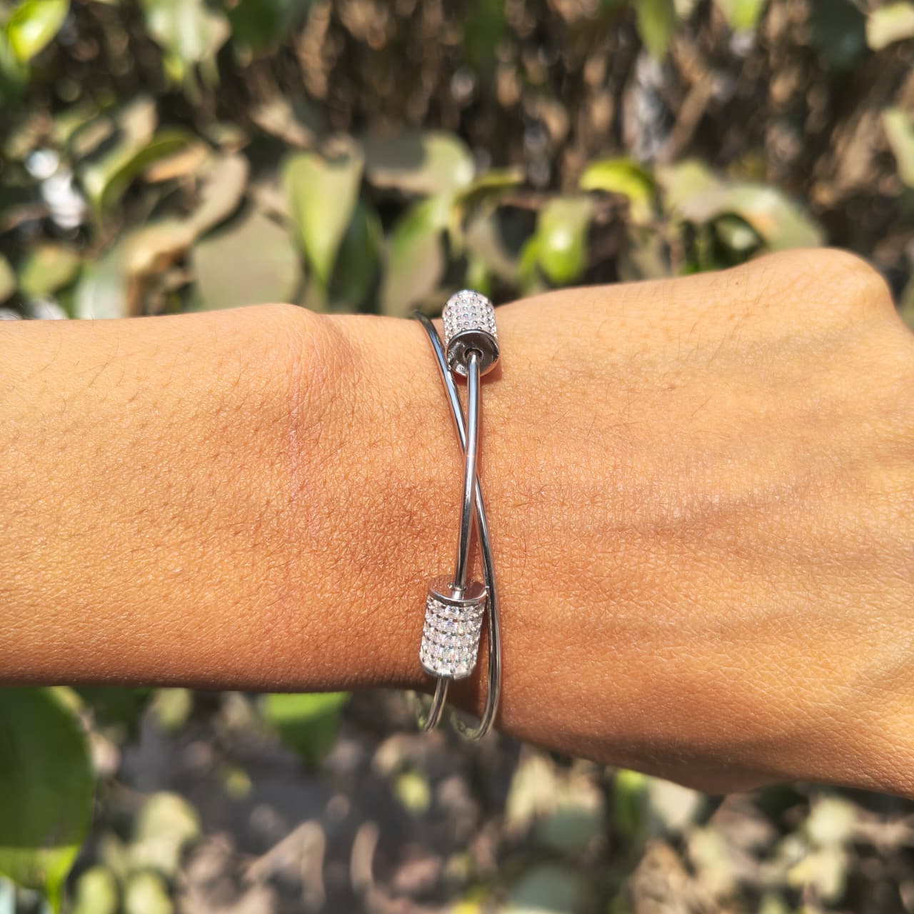 Silver bracelet with clear stones on a wrist against a blurred green background