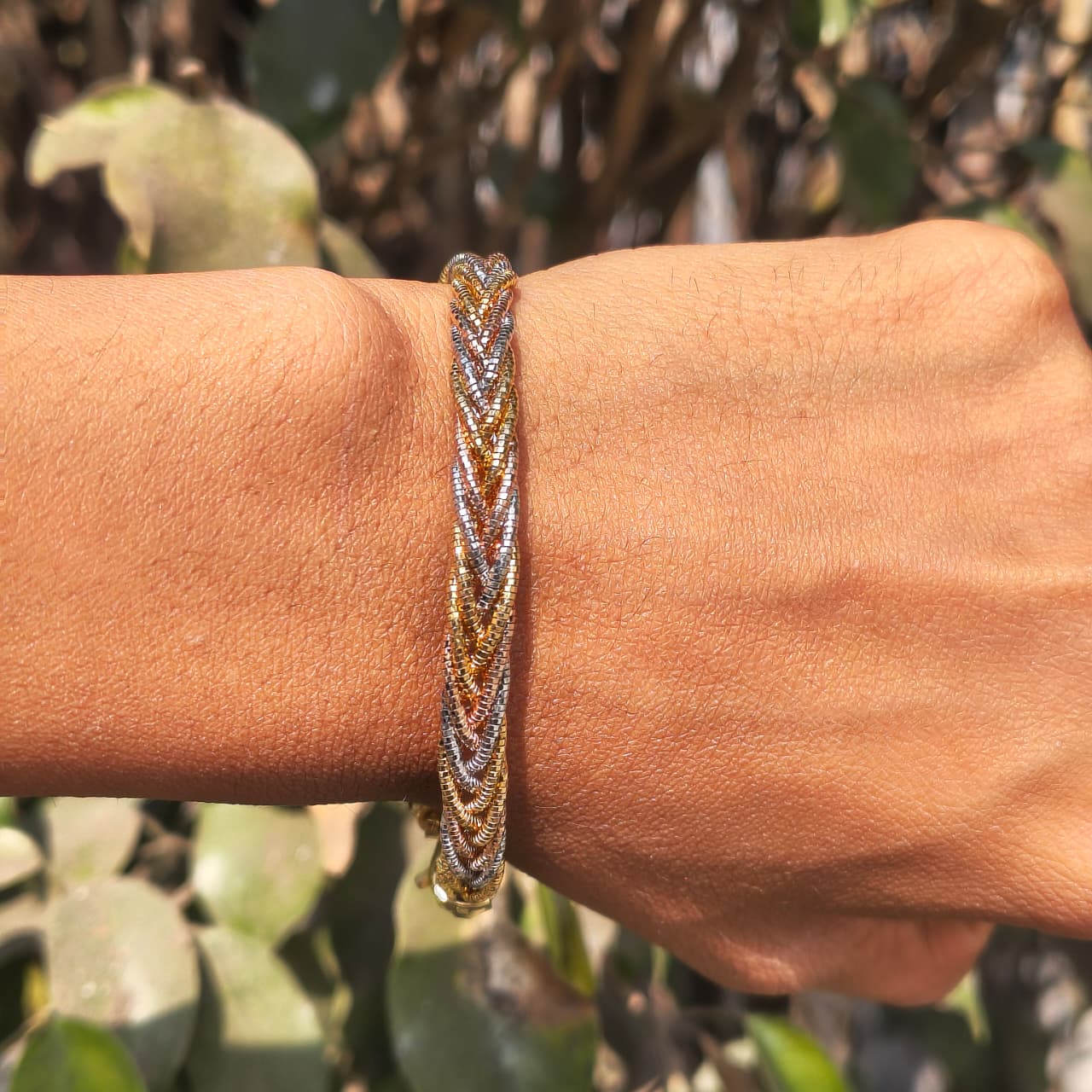 Close-up of a hand wearing a braided bracelet with a blurred green background