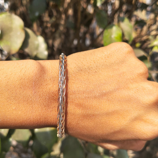 Silver braided bracelet on a wrist with a blurred green background