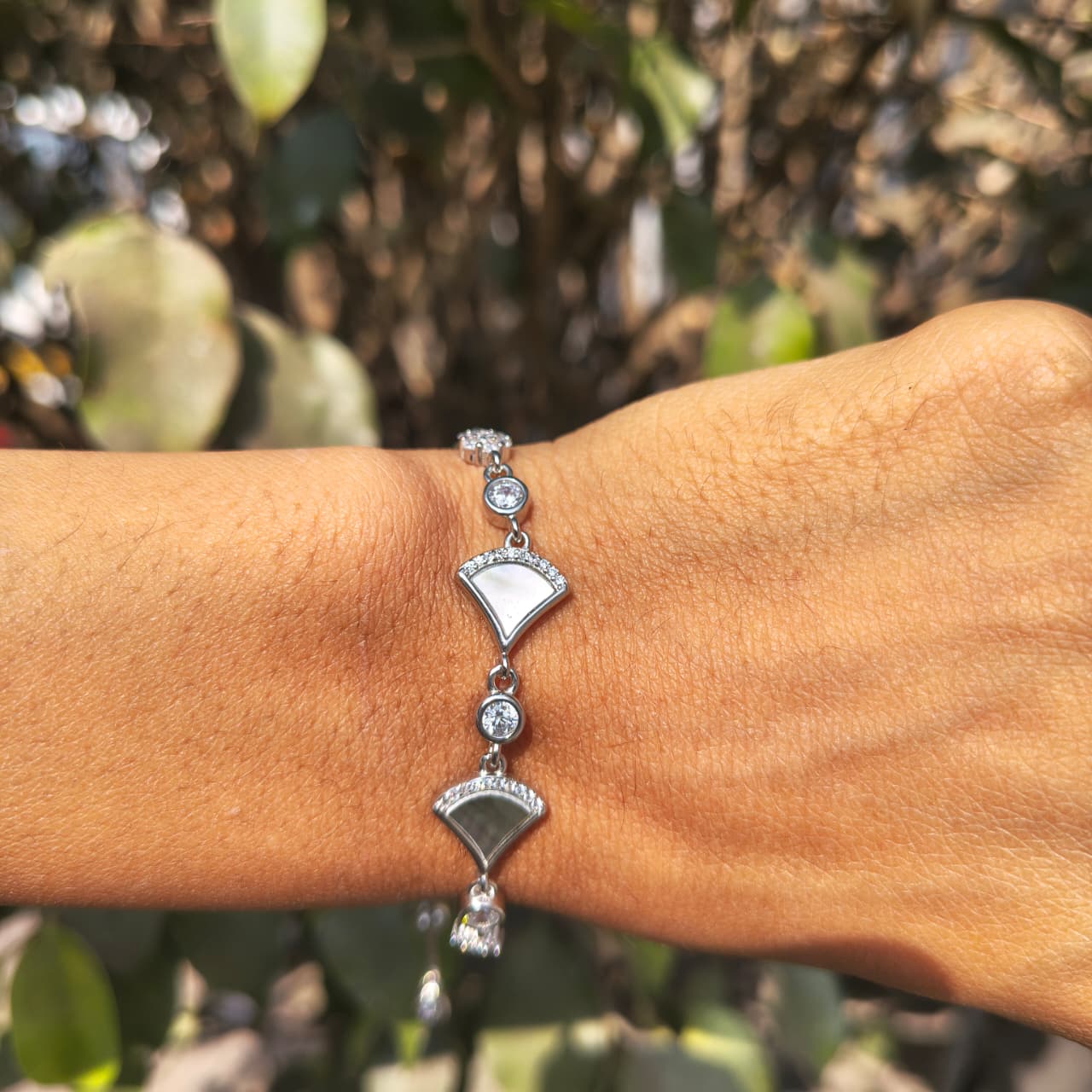 Silver bracelet on a wrist with a blurred green background
