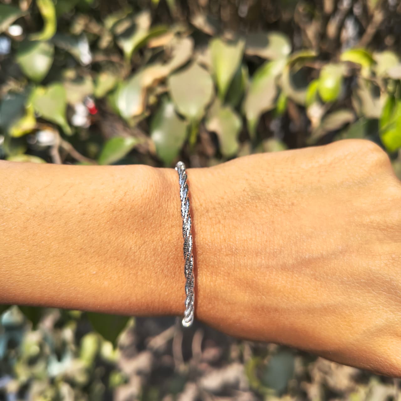 Silver bracelet on a wrist with a blurred green leafy background
