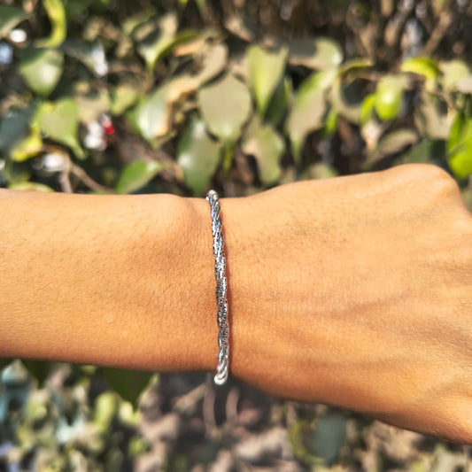 Silver bracelet on a wrist with a blurred green leafy background