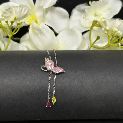 Butterfly-shaped necklace with gemstones on a black surface with white flowers in the background