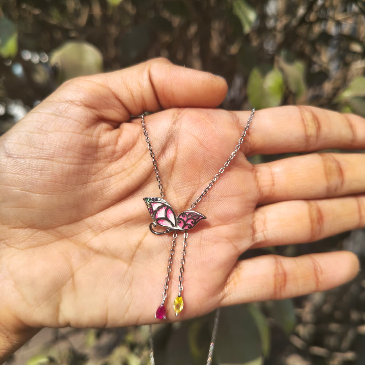 Butterfly necklace with colorful pendants held in a hand against a blurred natural background