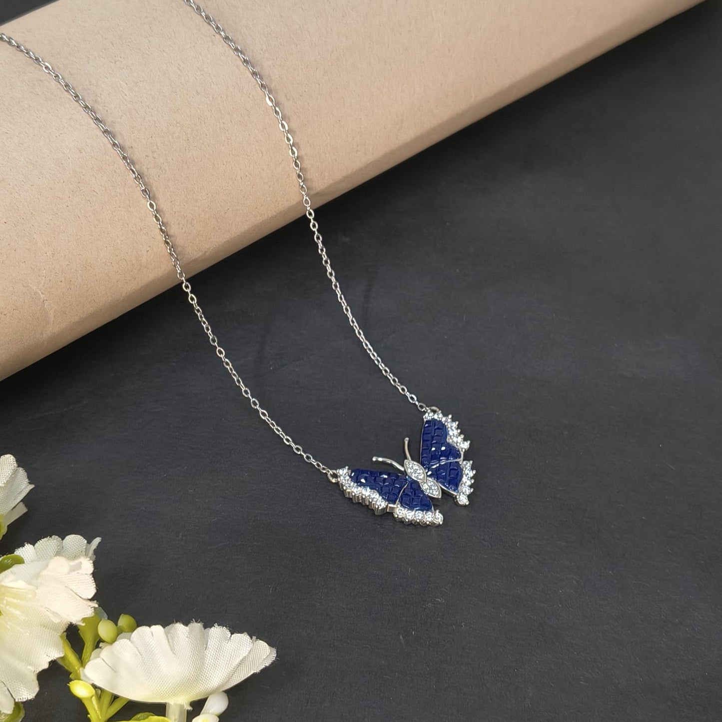 Butterfly-shaped necklace with blue stones on a dark surface with white flowers.