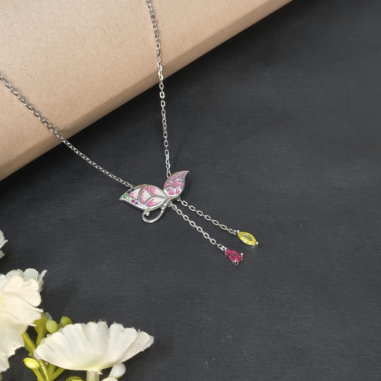 Butterfly necklace with gemstones on a dark surface with flowers