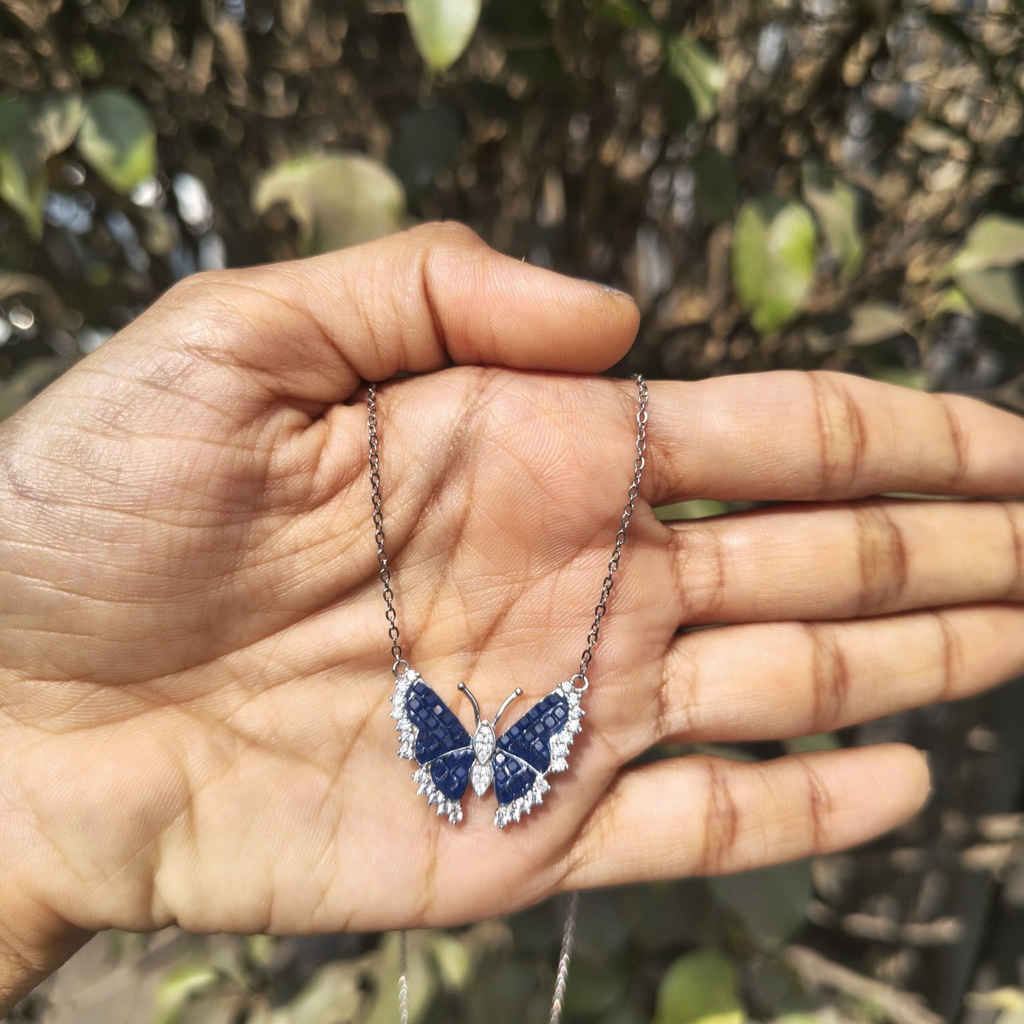 Butterfly-shaped necklace held in a hand with a natural background