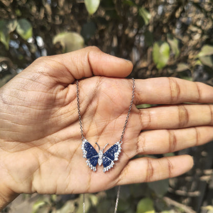 Butterfly-shaped necklace held in a hand with a natural background