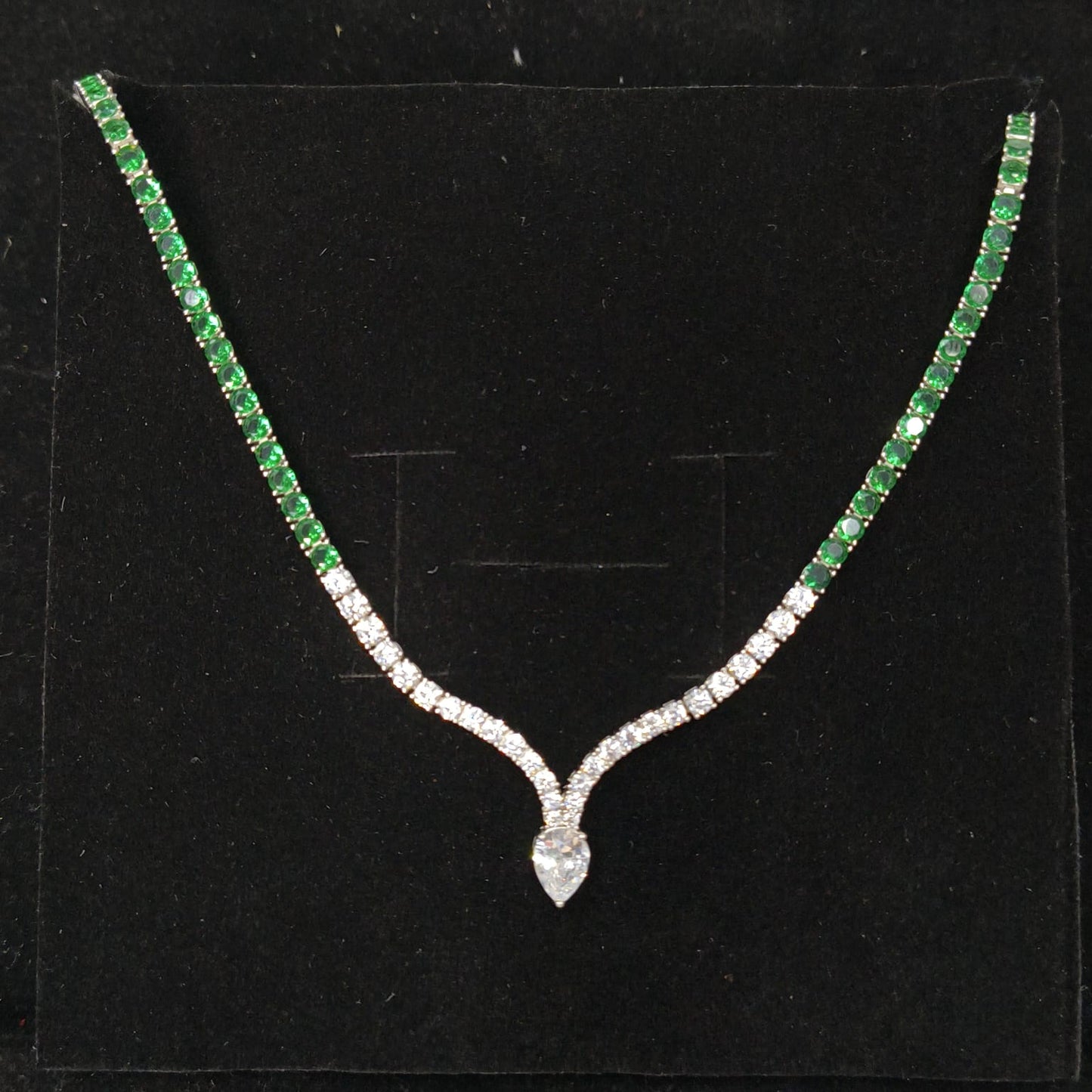 Necklace with green gemstones and a diamond pendant on a black background