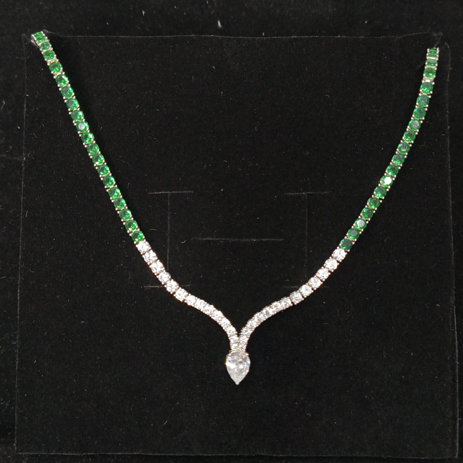 Necklace with green gemstones and a diamond pendant on a black background