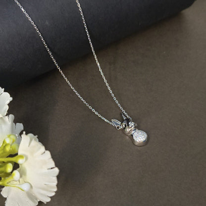 Silver necklace with a heart-shaped pendant on a dark surface with flowers.