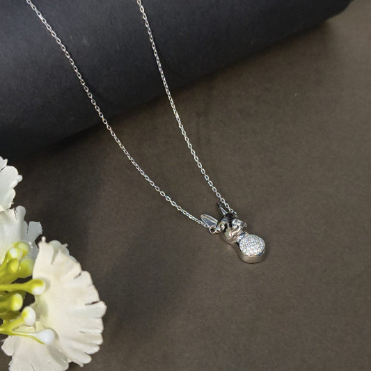 Silver necklace with a heart-shaped pendant on a dark surface with flowers.
