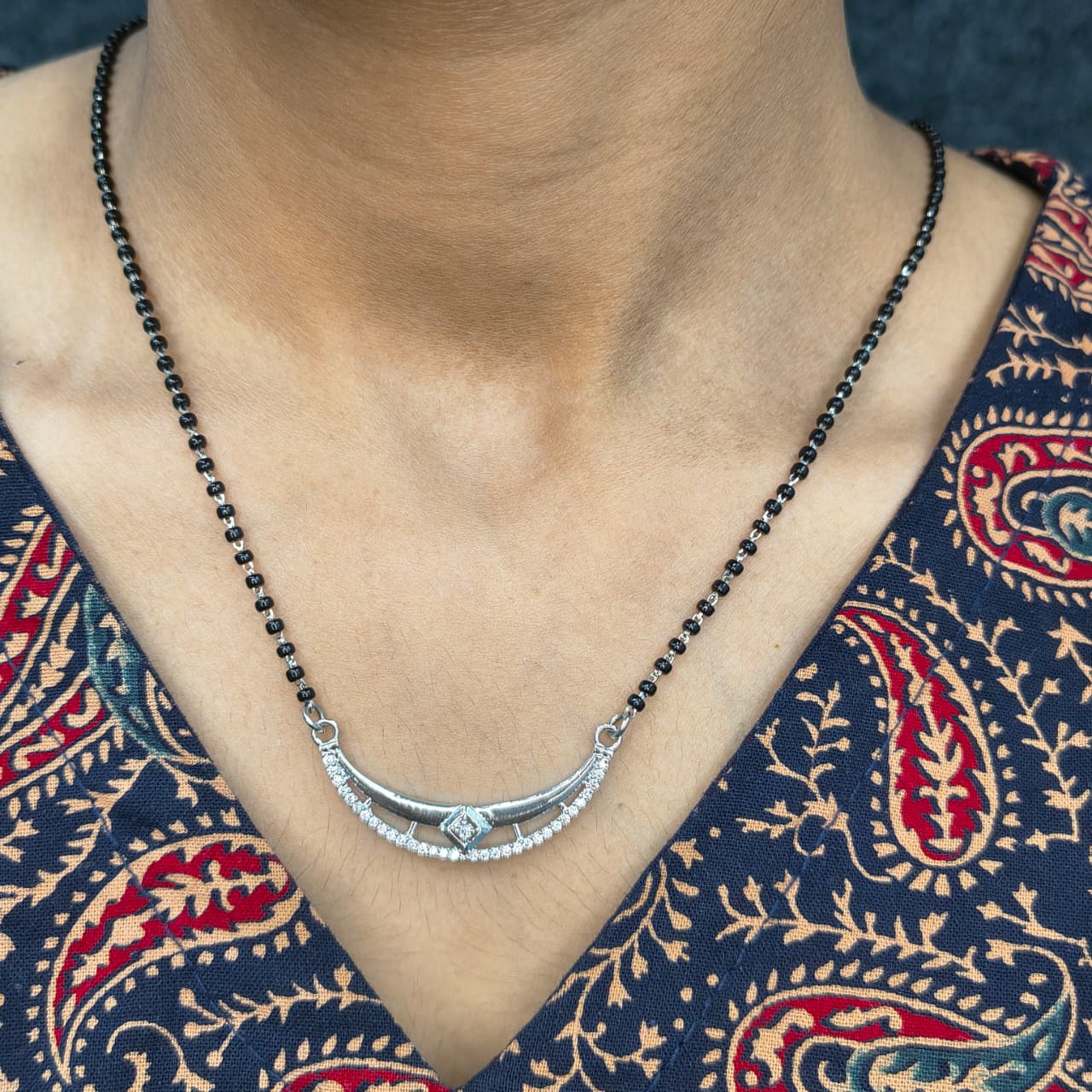 Necklace with black beads and silver pendant on a person wearing a patterned garment.