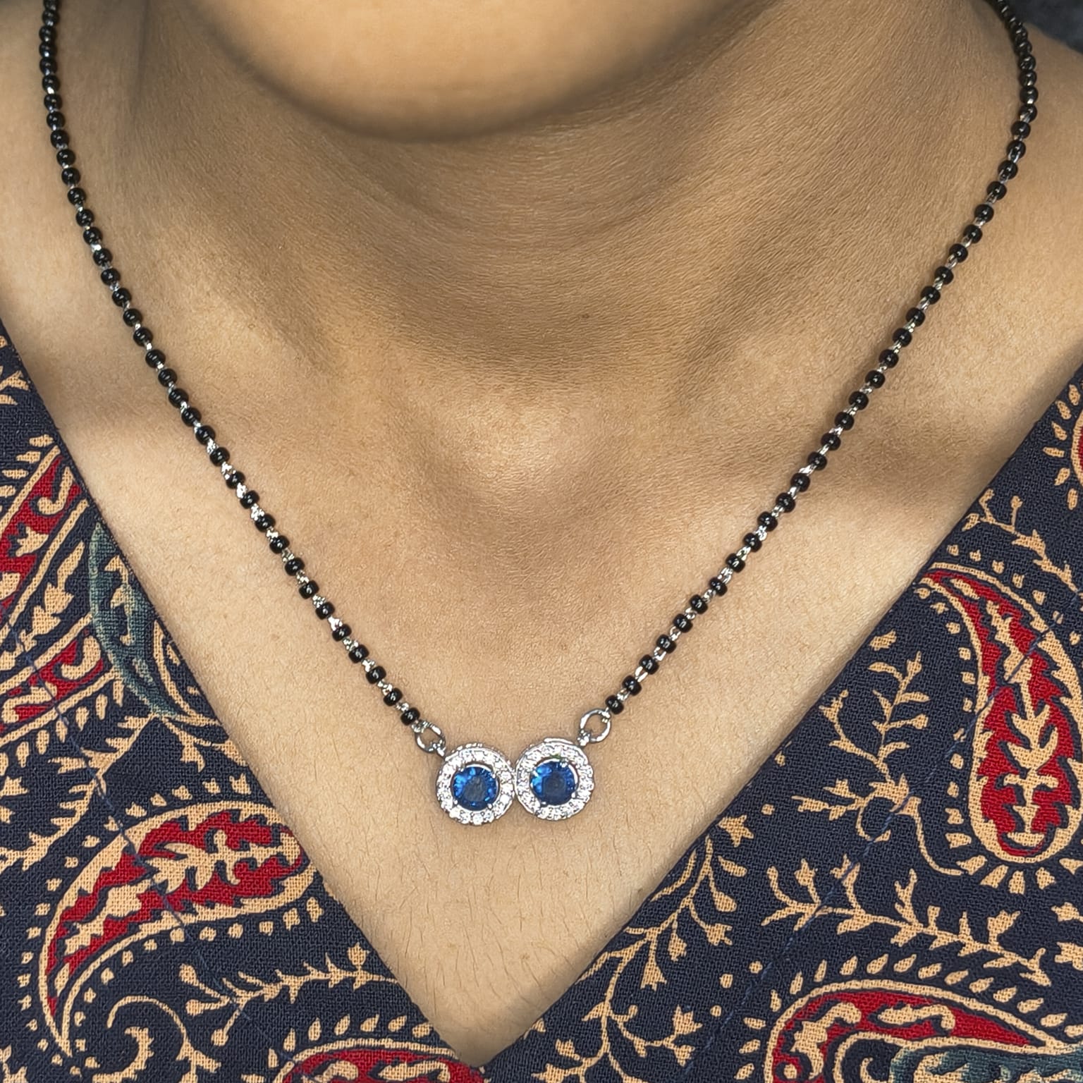 Necklace with blue gemstones worn by a person in a patterned garment
