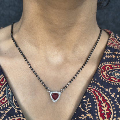 Necklace with a red gemstone pendant worn by a person against a patterned fabric background