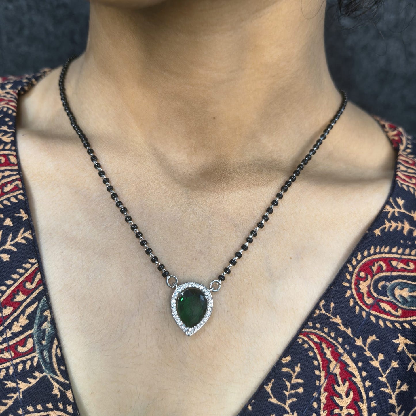 Necklace with a green pendant worn by a person against a dark background