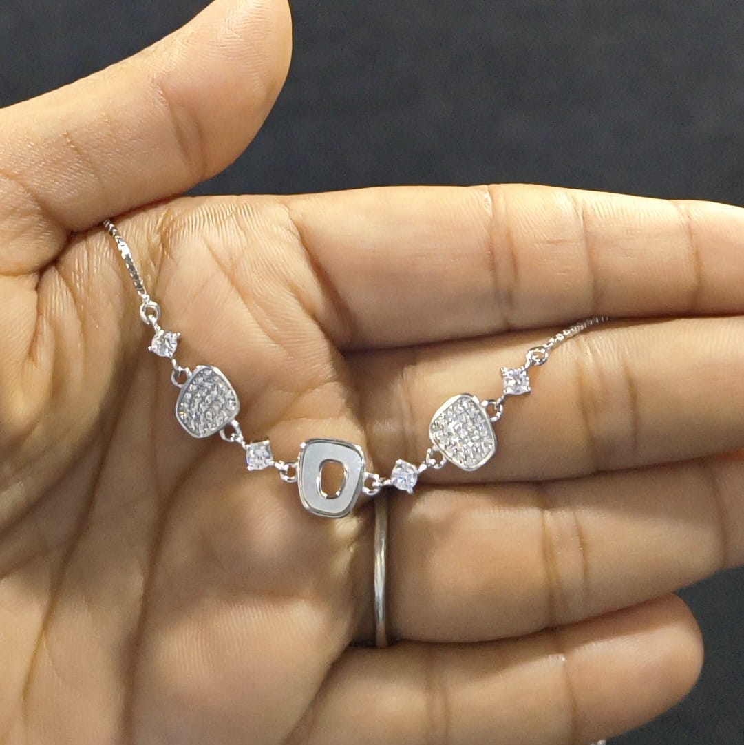 Silver bracelet with heart and circular designs held in a hand against a dark background