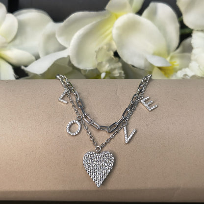 Silver bracelet with heart charm and 'LOVE' letters on a beige surface with white flowers in the background