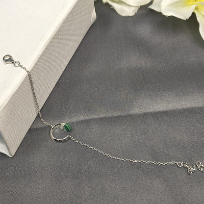 Silver bracelet with a green gemstone on a gray surface with white flowers in the background
