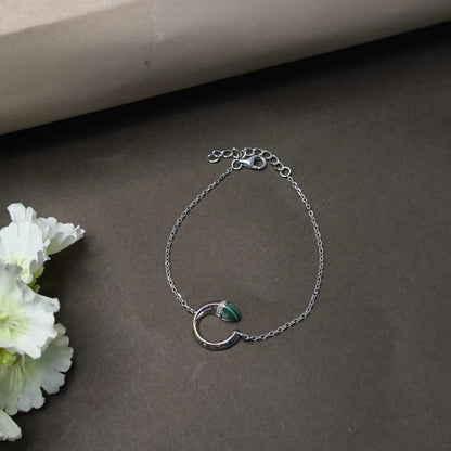 Silver bracelet with a green stone on a dark surface with flowers