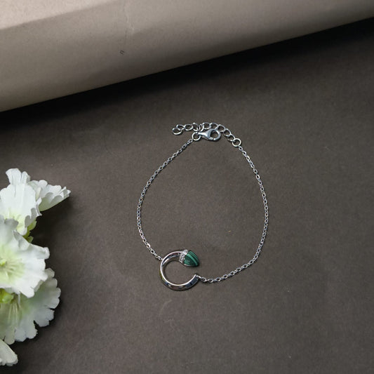 Silver bracelet with a green stone on a dark surface with flowers