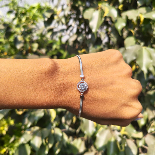 Silver bracelet with a circular design worn on a wrist against a blurred green leafy background
