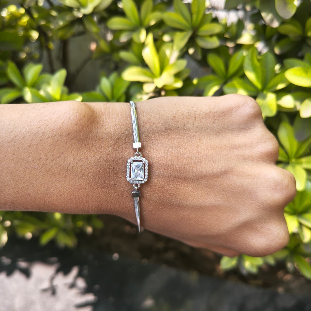Silver bracelet with a diamond on a wrist against a green leafy background