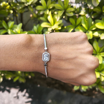 Silver bracelet with a diamond on a wrist against a green leafy background
