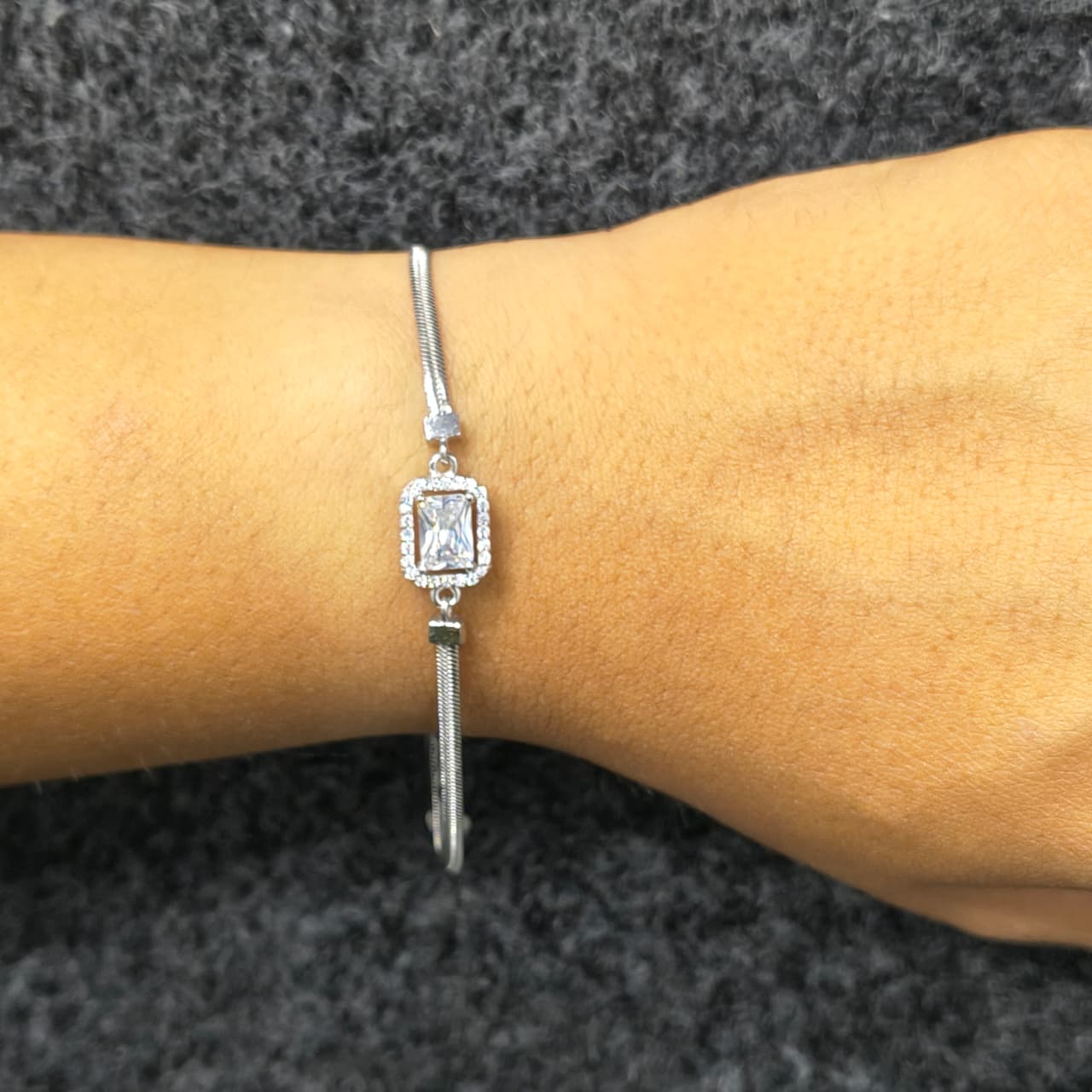 Silver bracelet with a decorative clasp on a wrist against a gray background