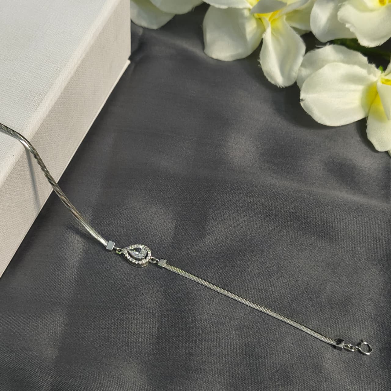 Silver bracelet on a dark fabric surface with white flowers in the background