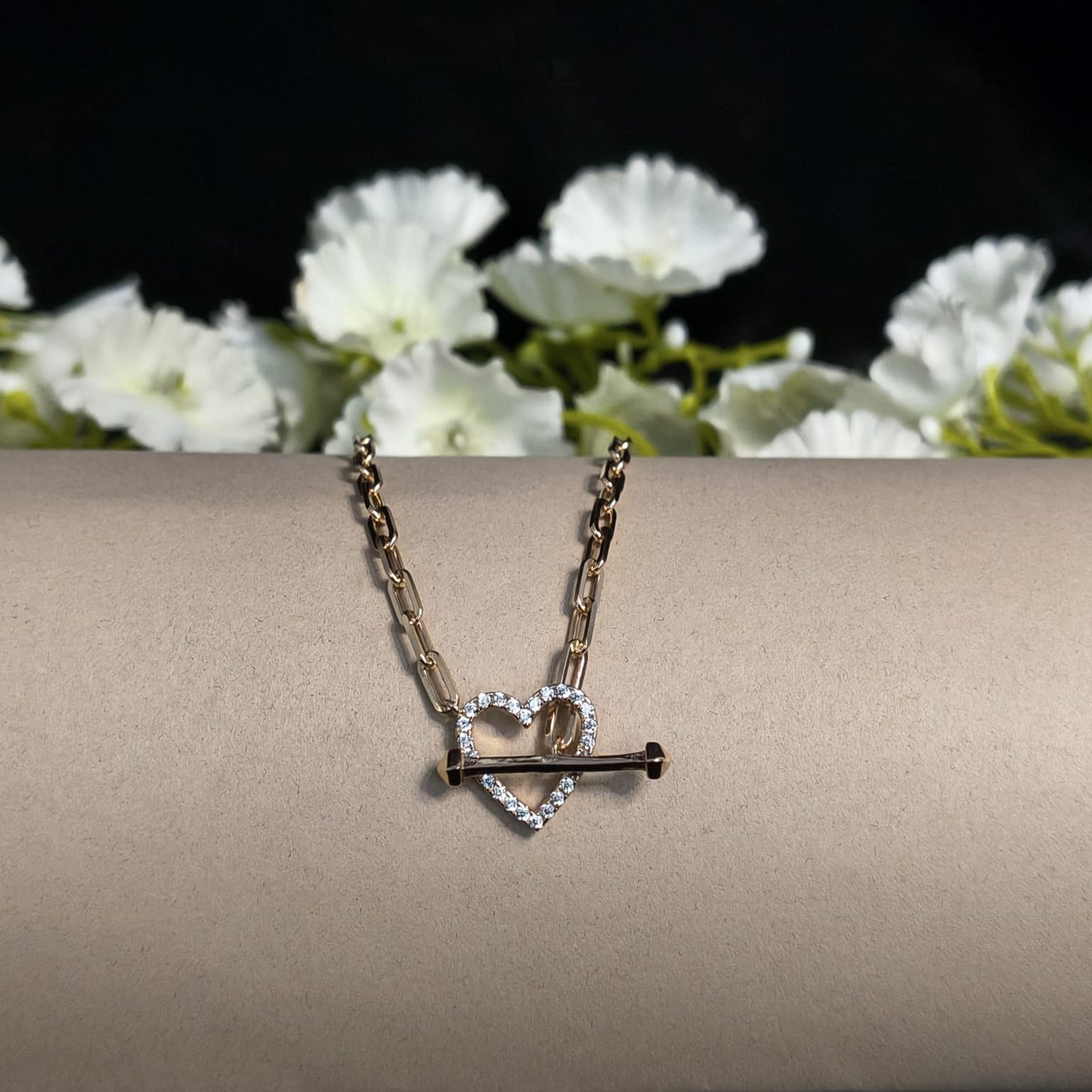 Necklace with heart and key pendant on a beige surface with white flowers in the background