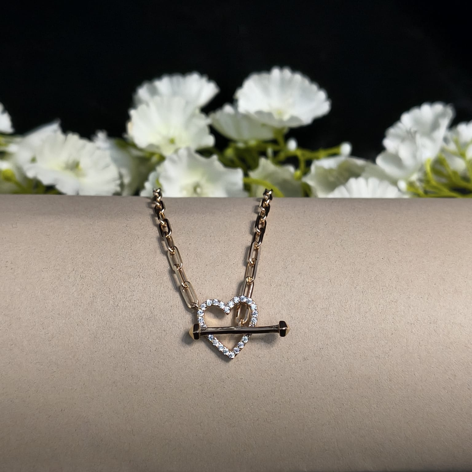 Necklace with heart and key pendant on a beige surface with white flowers in the background