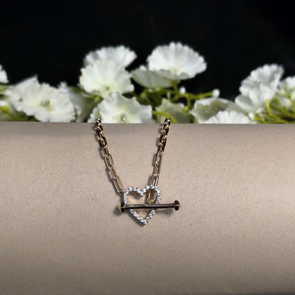 Necklace with heart and key pendant on a beige surface with white flowers in the background