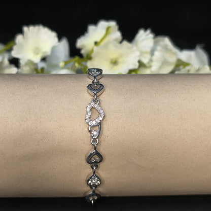 Silver bracelet with heart designs on a wrist against a dark background with white flowers.