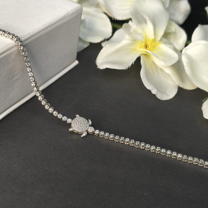 Silver bracelet with a turtle charm on a dark surface with white flowers in the background